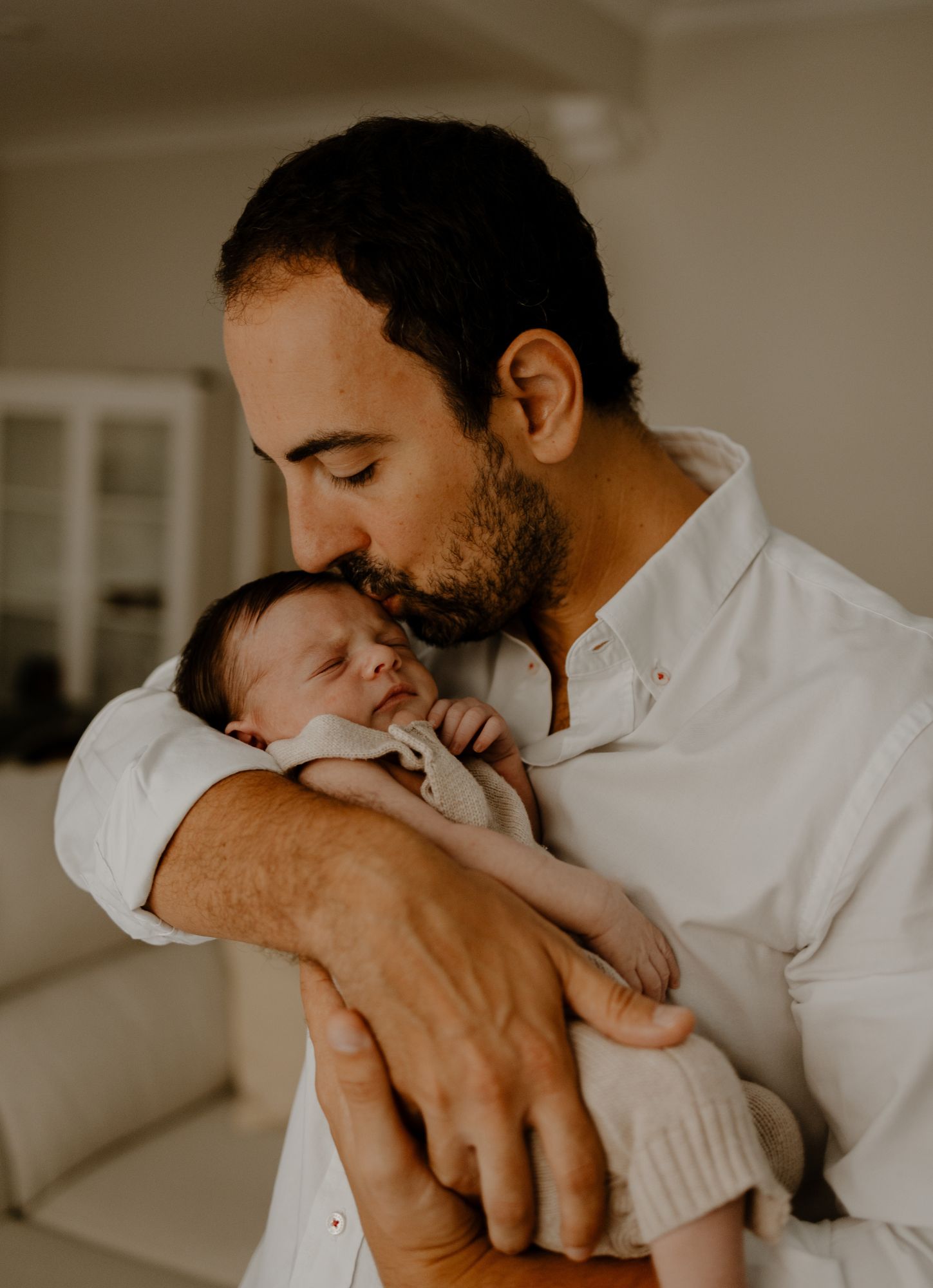 Padre cogiendo en brazos a su recién nacido, dándole un beso en la frente en su sesión newborn lifestyle